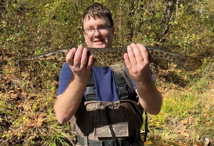 A reseacher holds up a spotted gar in both hands.